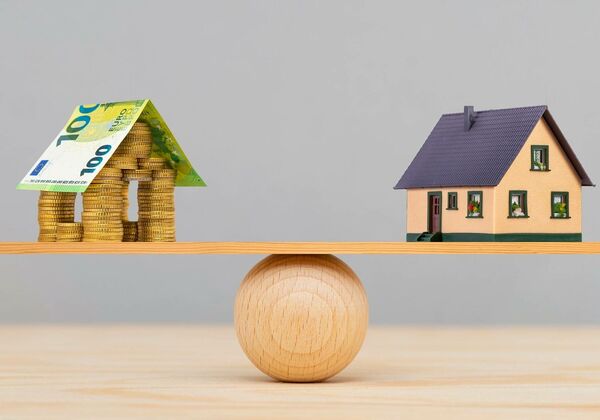 Geldscheine und ein Haus halten sich die Waage